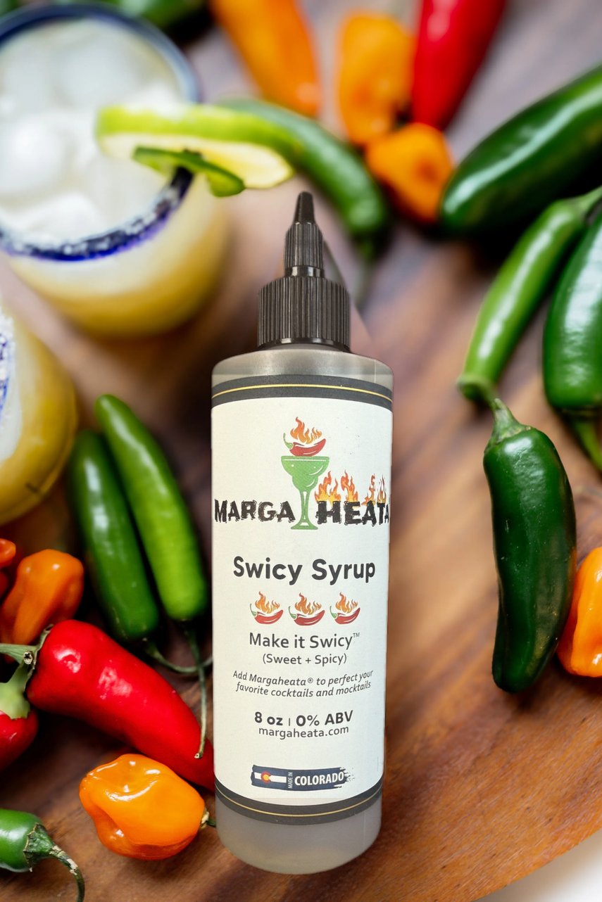 Margaheata® Swicy Syrup bottle surrounded by fresh serranos, habaneros, and jalapeños